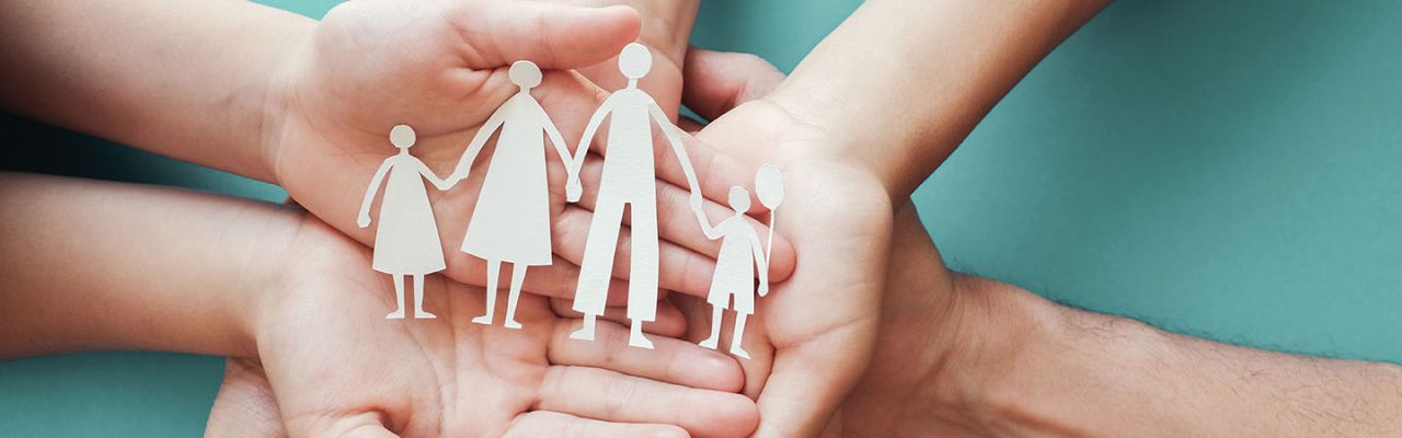 A group of clasped hands holding a paper machete of a family.