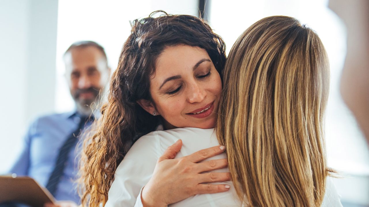 Two females hugging each other in a group therapy session.